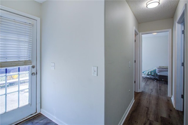 hallway with a textured ceiling, wood finished floors, and baseboards