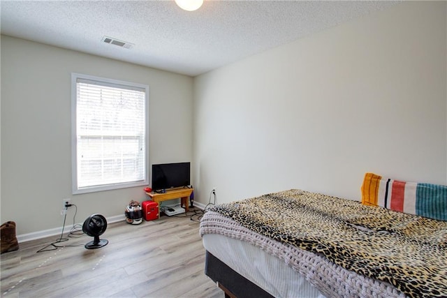 bedroom with light wood-style floors, visible vents, a textured ceiling, and baseboards