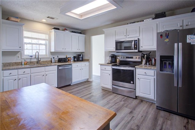 kitchen with stainless steel appliances, white cabinetry, a sink, and light wood finished floors