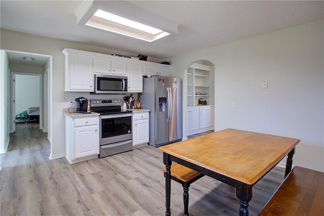 kitchen with arched walkways, stainless steel appliances, light wood-style floors, white cabinets, and light countertops