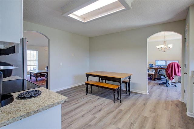 dining area with light wood-type flooring, baseboards, arched walkways, and a textured ceiling