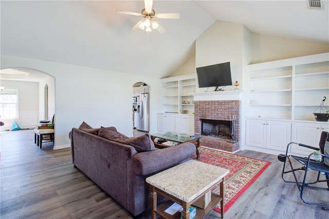 living room featuring visible vents, arched walkways, wood finished floors, built in shelves, and a fireplace