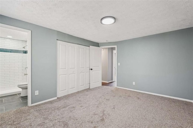 unfurnished bedroom featuring ensuite bath, a closet, a textured ceiling, and carpet flooring