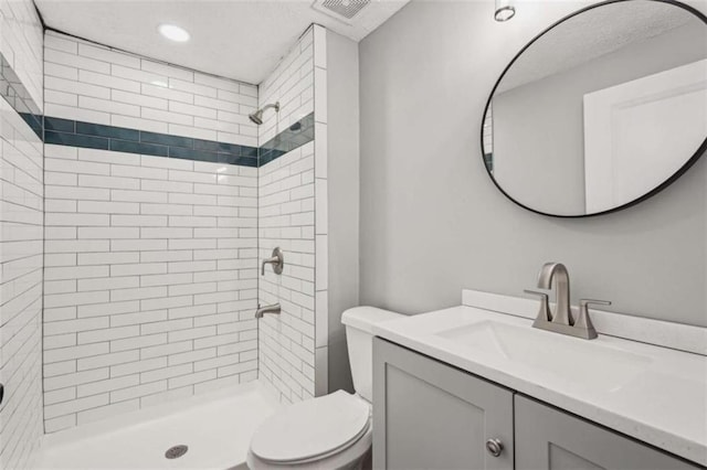 bathroom featuring vanity, a tile shower, and toilet