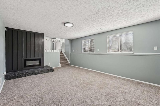 unfurnished living room featuring a stone fireplace, carpet, and a textured ceiling