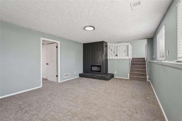 unfurnished living room featuring a large fireplace, carpet flooring, and a textured ceiling