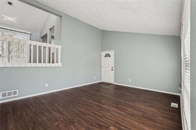 spare room with dark wood-type flooring, lofted ceiling, and a textured ceiling