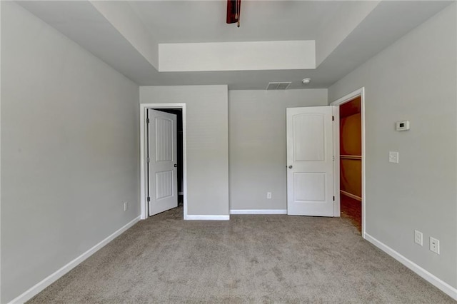 unfurnished bedroom featuring a raised ceiling, a walk in closet, and light colored carpet