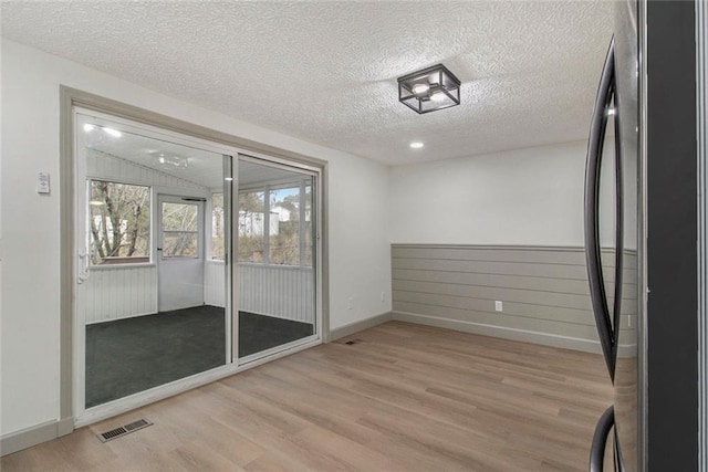 empty room with lofted ceiling, visible vents, light wood-style flooring, and a textured ceiling