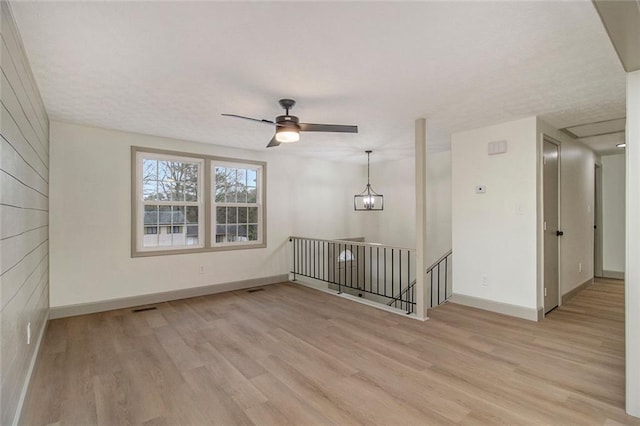 empty room featuring baseboards, ceiling fan with notable chandelier, visible vents, and light wood-style floors