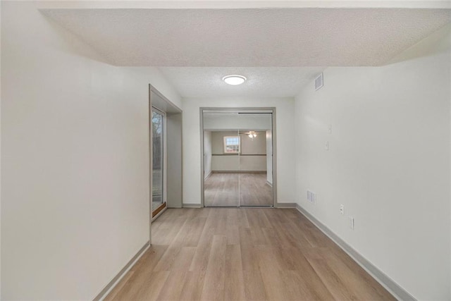 hall featuring light wood-type flooring, visible vents, a textured ceiling, and baseboards