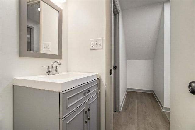 bathroom with baseboards, vaulted ceiling, wood finished floors, and vanity