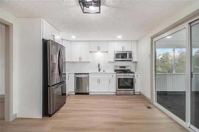 kitchen with stainless steel appliances, visible vents, a sink, and light wood finished floors