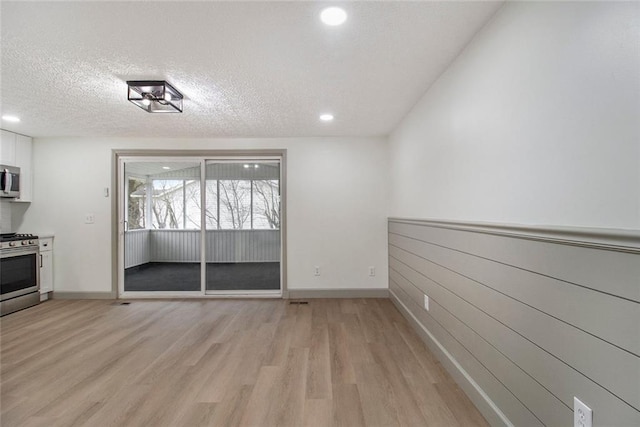 unfurnished dining area with light wood-style floors, baseboards, a textured ceiling, and recessed lighting