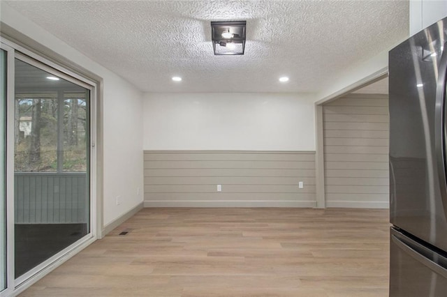 empty room with recessed lighting, wainscoting, a textured ceiling, and light wood finished floors