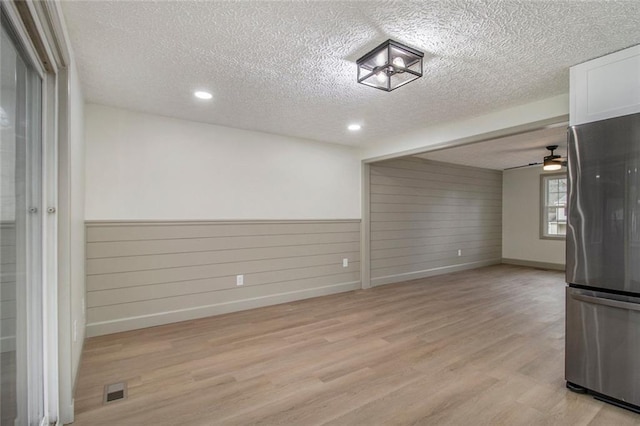 empty room with a wainscoted wall, visible vents, light wood-style flooring, ceiling fan, and a textured ceiling