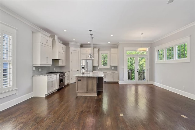 kitchen with dark hardwood / wood-style floors, light stone counters, hanging light fixtures, a center island with sink, and stainless steel appliances