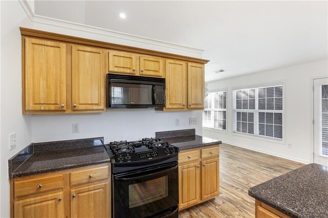 kitchen with dark stone countertops, crown molding, black appliances, and light wood-type flooring