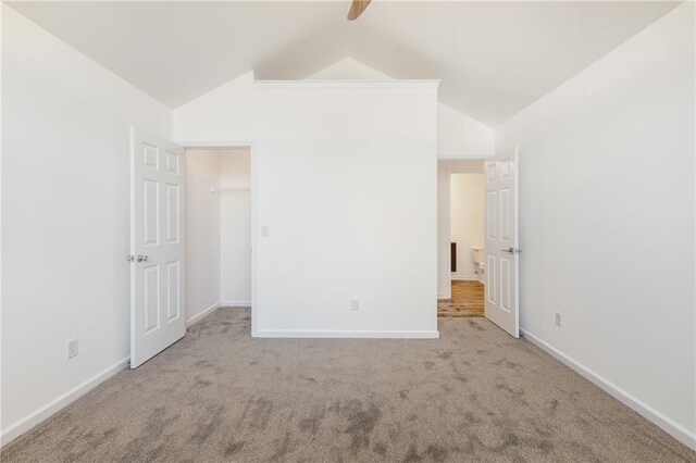 unfurnished bedroom with ceiling fan, a walk in closet, light carpet, and vaulted ceiling