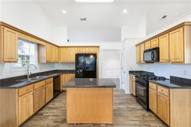 kitchen with black appliances, sink, hardwood / wood-style flooring, a towering ceiling, and a kitchen island