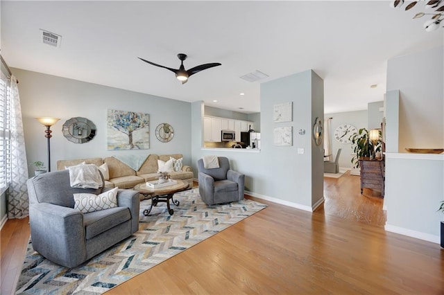 living area featuring baseboards, ceiling fan, wood finished floors, and visible vents