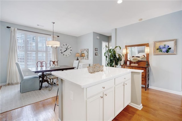 kitchen with a kitchen island, baseboards, white cabinetry, light wood finished floors, and decorative light fixtures