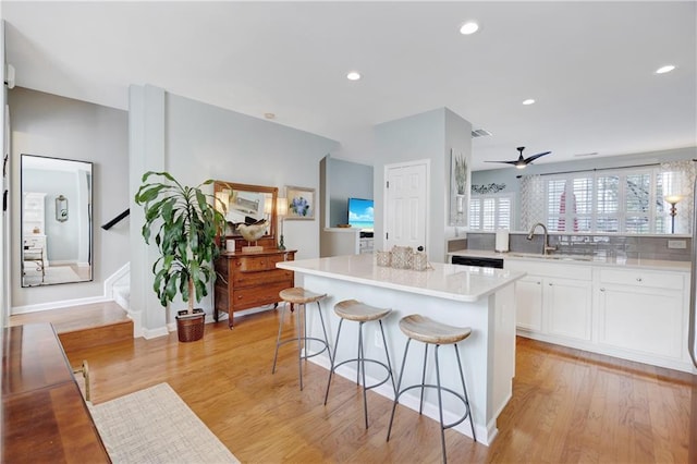 kitchen featuring ceiling fan, a breakfast bar, light countertops, white cabinetry, and a kitchen island