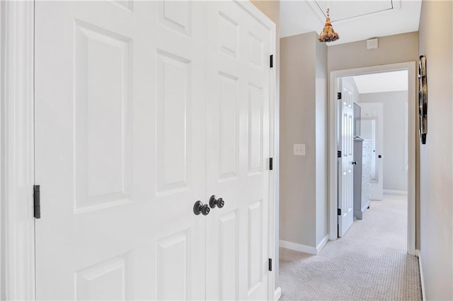 corridor with light colored carpet, attic access, and baseboards