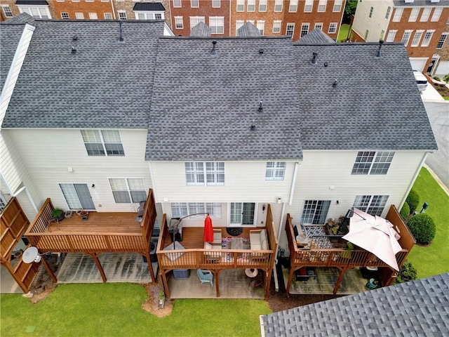 rear view of property featuring roof with shingles, a yard, and a deck