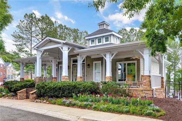 view of front facade with ceiling fan, fence, covered porch, stone siding, and roof with shingles