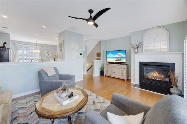 living area featuring a glass covered fireplace, baseboards, ceiling fan, and wood finished floors