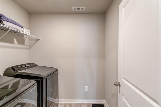 laundry area featuring visible vents, baseboards, laundry area, wood finished floors, and separate washer and dryer