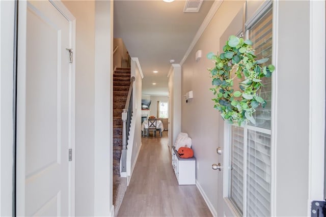 corridor featuring visible vents, crown molding, baseboards, stairway, and light wood-style flooring