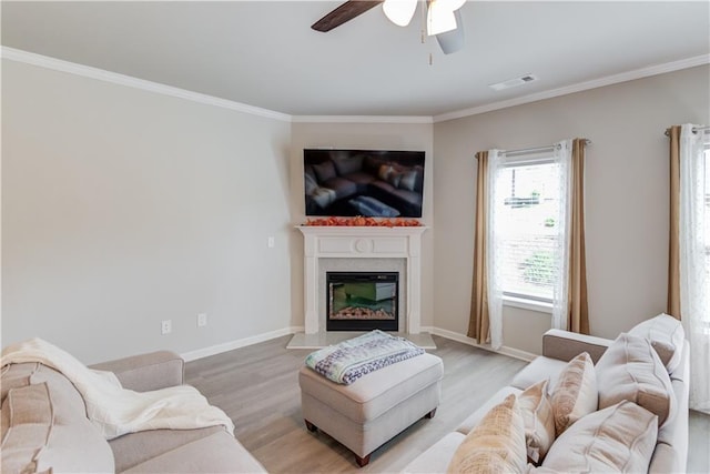 living area with a glass covered fireplace, crown molding, light wood-style flooring, and visible vents