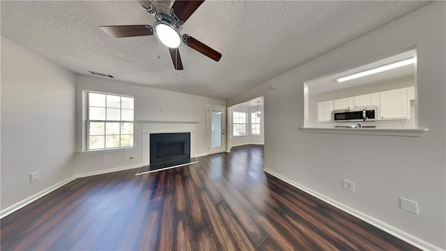 unfurnished living room featuring a wealth of natural light, visible vents, dark wood-type flooring, and a fireplace