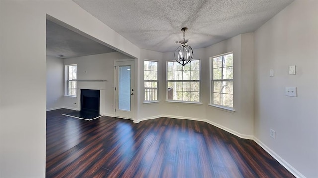 unfurnished living room featuring baseboards, plenty of natural light, a fireplace with raised hearth, and dark wood-style floors