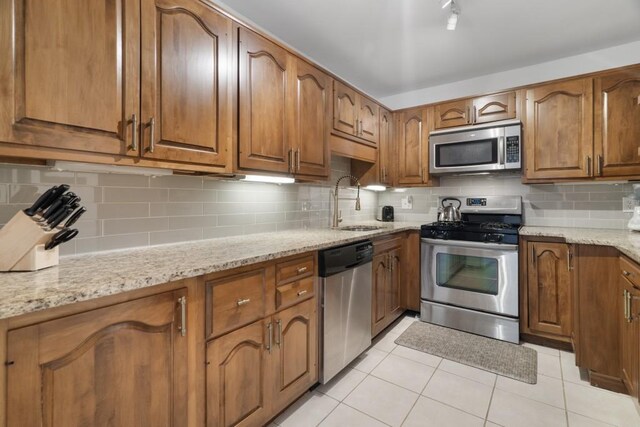 kitchen with appliances with stainless steel finishes, light stone counters, sink, light tile patterned flooring, and tasteful backsplash