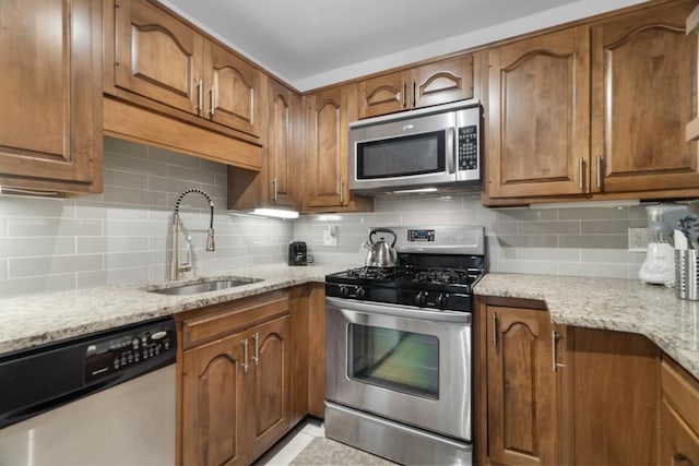 kitchen featuring sink, backsplash, light stone counters, and appliances with stainless steel finishes