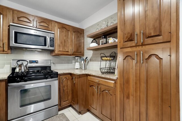 kitchen featuring light stone countertops, light tile patterned floors, tasteful backsplash, and appliances with stainless steel finishes