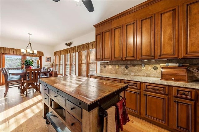 kitchen featuring ceiling fan with notable chandelier, decorative light fixtures, tasteful backsplash, light stone counters, and light wood-type flooring