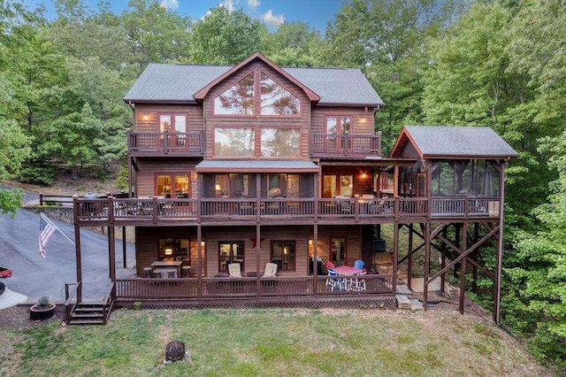 rear view of house with a balcony, a sunroom, a deck, and a lawn