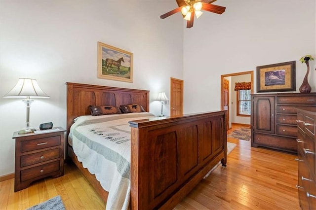 bedroom featuring ceiling fan, a towering ceiling, and light wood-type flooring