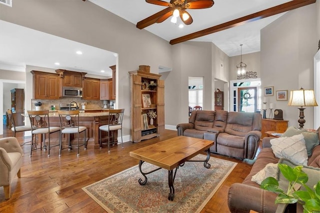 living room featuring dark wood-type flooring, sink, beamed ceiling, ceiling fan with notable chandelier, and a high ceiling