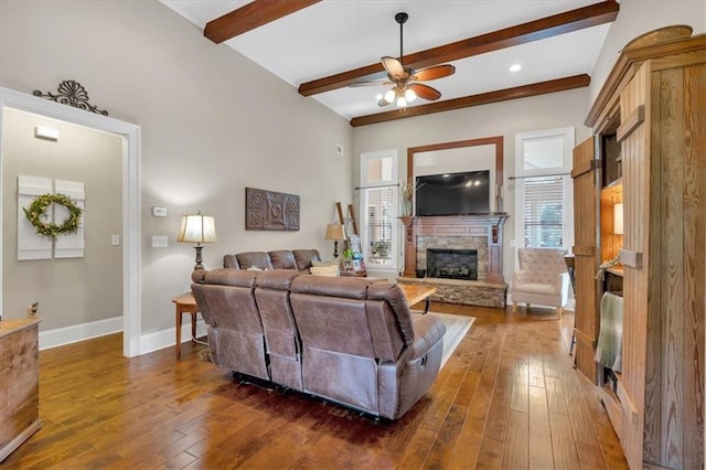 living room with ceiling fan, a stone fireplace, dark hardwood / wood-style floors, and beamed ceiling