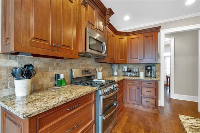 kitchen featuring dark wood-type flooring, backsplash, stainless steel appliances, light stone countertops, and ornamental molding