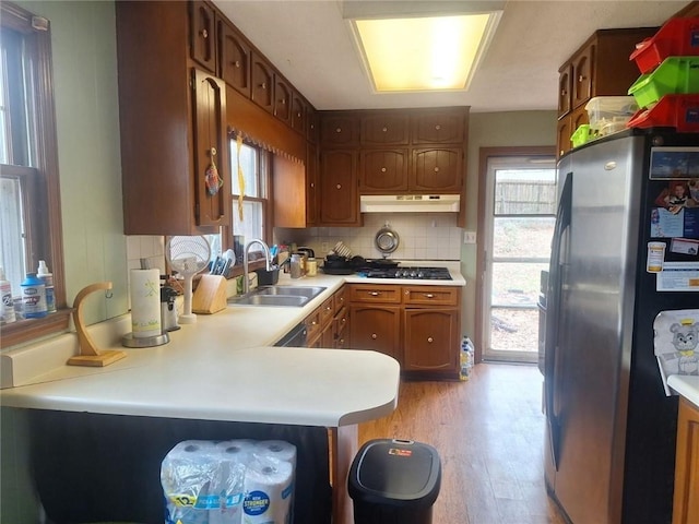 kitchen featuring stainless steel fridge, under cabinet range hood, a sink, light wood-type flooring, and light countertops