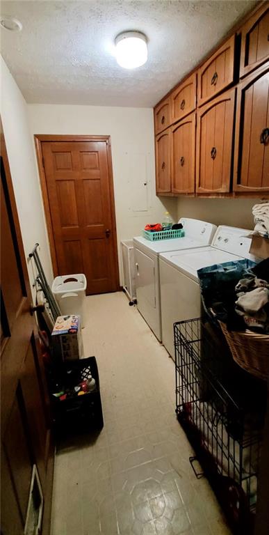 laundry room with washer and clothes dryer, cabinet space, and a textured ceiling