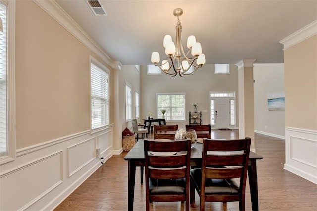 dining space with a notable chandelier, dark wood-type flooring, ornamental molding, and decorative columns