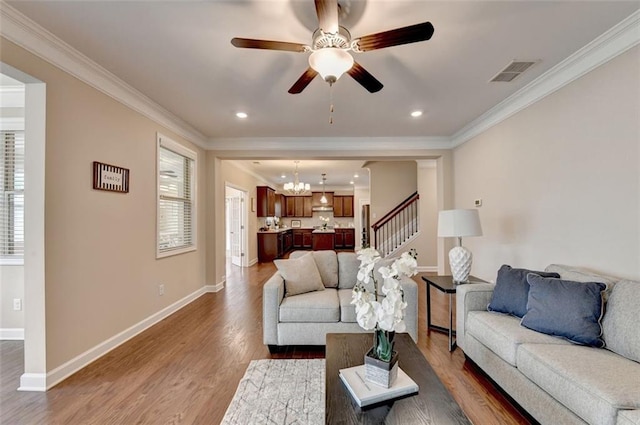 living room featuring ceiling fan with notable chandelier, wood-type flooring, and ornamental molding