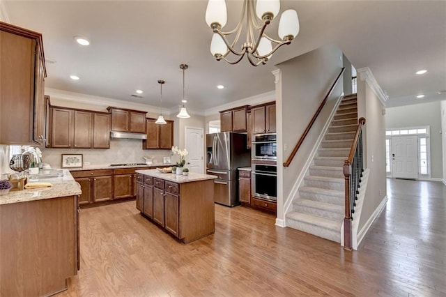 kitchen with a kitchen island, decorative light fixtures, sink, stainless steel appliances, and light stone countertops